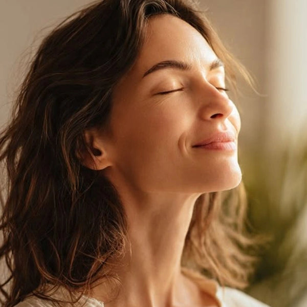 A side profile portrait of a woman with her eyes closed and a gentle smile, basking in soft, warm sunlight