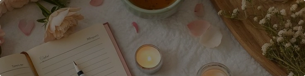 An open notebook sits on a soft surface next to a fountain pen. A lit candle in a small glass container glows nearby